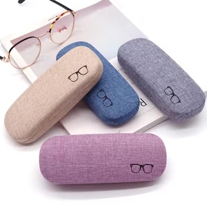 Pode incluir: Quatro estojos para óculos de tecido de diferentes cores com um ícone de óculos em cada um. Os estojos são bege, azul, cinza e roxo.