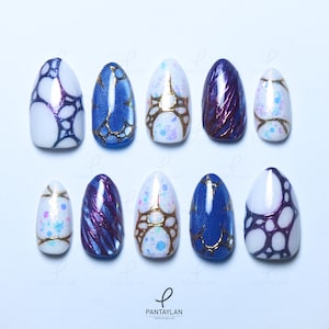 May include: A set of ten almond-shaped press-on nails featuring various designs including white with dark purple bubble patterns, blue with gold veining, white with iridescent glitter and gold lines, and deep purple with metallic textured streaks.