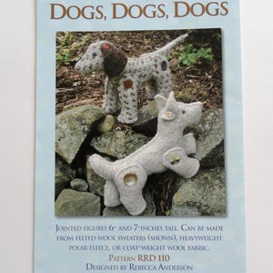 May include: A sewing pattern booklet titled Rebecca Ruth Designs DOGS, DOGS, DOGS featuring two jointed dog figures, one spotted and one solid light gray, with button joints. The text indicates jointed figures 6 and 7 inches tall.