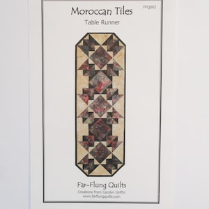 May include: A printed paper featuring a table runner design titled "Moroccan Tiles." The runner design is a geometric pattern in shades of red, black, and beige. The text "Far-Flung Quilts" and website address are also visible.