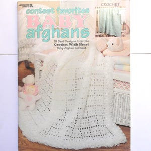 May include: A magazine cover titled "contest favorites BABY afghans" featuring a white crocheted baby blanket. The cover also shows a crocheted blanket and a stuffed animal. The text reads "19 Best Designs from the Crochet With Heart Baby Afghan Contest."