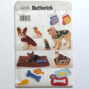 May include: A Butterick sewing pattern, number 4226, featuring various pet accessories. The pattern includes instructions for dog coats, pet beds, stockings, and toys. The image shows examples of the finished products, including a red plaid dog coat and a cat bed.