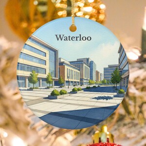 Puede incluir: Adorno navideño redondo de cerámica con una ilustración en acuarela de una escena de la calle de la ciudad. La imagen muestra edificios modernos, árboles y una pasarela pavimentada bajo un cielo azul. La palabra "Waterloo" está impresa en la parte superior.