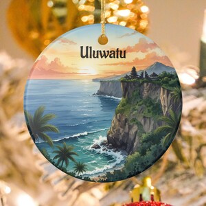 Peut inclure: Ornement rond en céramique représentant une scène côtière avec le texte "Uluwatu". Le design montre un coucher de soleil sur l'océan, des falaises et des palmiers. L'ornement a une ficelle dorée pour l'accrocher.