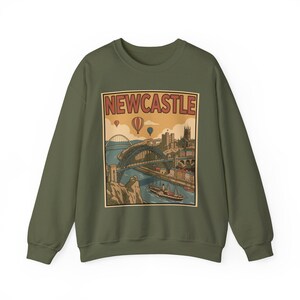 May include: Olive green sweatshirt featuring a vintage-style graphic of Newcastle, England. The design includes a bridge, buildings, hot air balloons, and the word "NEWCASTLE" in a rectangular frame. A stylish and comfortable garment for fans of the city.
