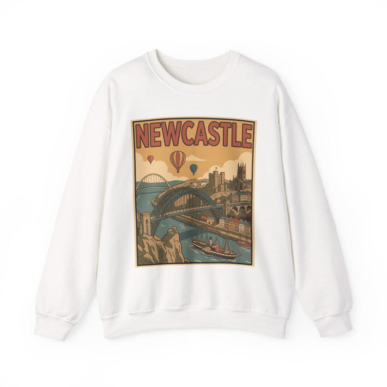 May include: White sweatshirt featuring a vintage-style illustration of Newcastle, England. The graphic includes a bridge, buildings, hot air balloons, and the word "NEWCASTLE" in a retro font. A cozy, casual top.