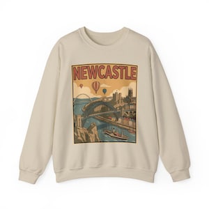 Retro graphic on a sand-colored sweatshirt showing the Newcastle landscape with the Tyne Bridge and hot air balloons.