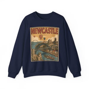 May include: Navy blue sweatshirt featuring a vintage-style illustration of Newcastle, with a bridge, buildings, and hot air balloons. The word "NEWCASTLE" is printed at the top of the design in a retro font. A classic crew neck sweatshirt.