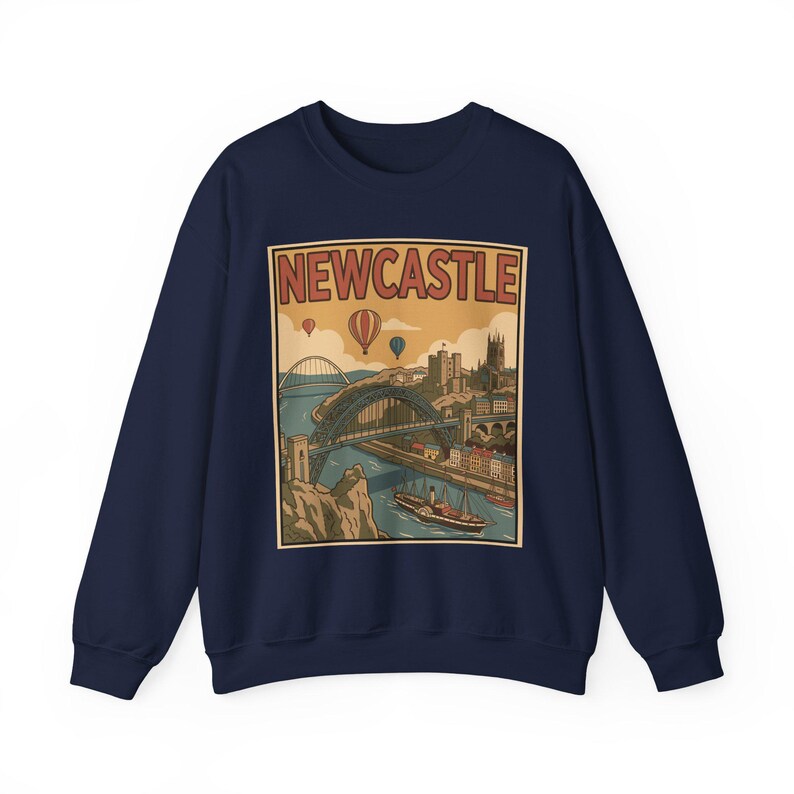 May include: Navy blue sweatshirt featuring a vintage-style illustration of Newcastle, with a bridge, buildings, and hot air balloons. The word "NEWCASTLE" is printed at the top of the design in a retro font. A classic crew neck sweatshirt.