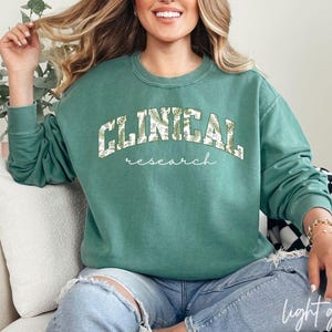 May include: A light green sweatshirt with the text "CLINICAL research" in white with a green and white leaf pattern.