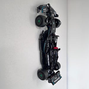 Puede incluir: Modelo LEGO negro y turquesa de un coche de carreras de Fórmula 1 con la marca Petronas. El coche está sobre un fondo blanco.