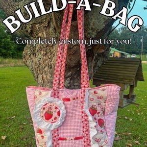 May include: Pink and white quilted tote bag with strawberry accents and red gingham straps. The bag features the text "BUILD-A-BAG" and "Completely custom, just for you!"