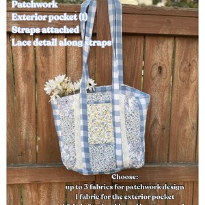 May include: A patchwork tote bag with blue and white gingham and floral patterns. Features include an exterior pocket, attached straps, and lace detail. The bag is filled with white flowers and has the text "EXAMPLE BAG".