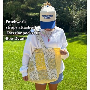 May include: A patchwork tote bag with attached straps and an exterior pocket. The bag features a mix of floral and gingham patterns in yellow and white. The text "EXAMPLE BAG" is at the top. The text "PATRIOTISM IS SEXY" is on a blue and white baseball cap.
