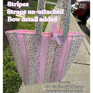 May include: A handmade tote bag with a floral and gingham pattern. The bag features pink stripes, unattached straps, and a bow detail. The text "EXAMPLE BAG" and other details are visible.