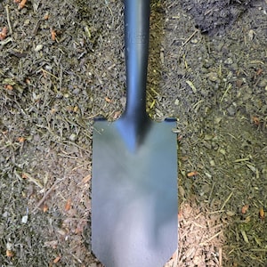 May include: A garden shovel with a matte black metal blade and a wooden handle. The shovel features a pointed tip and a smooth, dark finish on the metal head, which is securely attached to a light-colored wooden shaft for digging in soil.