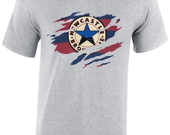 Puede incluir: Una camiseta gris con un diseño desgastado y rasgado que presenta el logotipo del Newcastle United Football Club. El logotipo es un círculo con una estrella y las palabras "Newcastle United" alrededor.