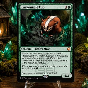 Puede incluir: Una carta coleccionable Badgermole Cub con borde verde, que presenta la ilustración de una criatura marrón y blanca en una cueva oscura llena de cristales. El texto de la carta incluye mecánicas de juego, el nombre Badgermole Cub y la frase Every mountain starts as a molehill.