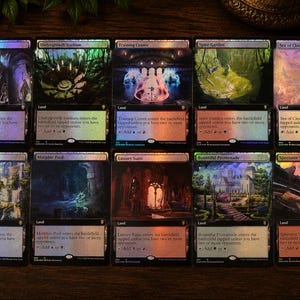 以下が含まれることがあります： 2列に並べられた10枚の長方形のMagic: The Gatheringトレーディングカード。各カードはホログラフィックフォイル仕上げで、詳細なファンタジー風景のイラストと、カード名やゲームルールを含む印刷されたテキストが特徴です。