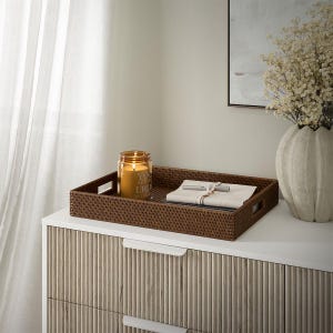 May include: A brown wicker tray with a candle and a notebook on a white dresser with brown wood drawer fronts. The candle is in a clear glass jar with the text "You are the light in this world" on it.