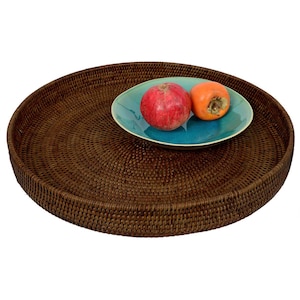 Könnte beinhalten: Ein rundes braunes Weidengeflecht-Serviertablett mit einer blauen und grünen Keramik Schale, die einen roten Apfel und eine orangefarbene Frucht enthält.