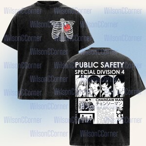 Può includere: T-shirt nero con effetto invecchiato, con un design a gabbia toracica e cuore rosso sul davanti. Il retro presenta "PUBLIC SAFETY SPECIAL DIVISION 4" con illustrazioni in stile anime e testo giapponese.