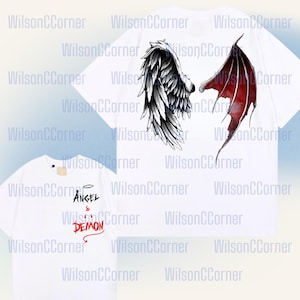 May include: White t-shirts featuring angel and demon wing designs. One shirt displays a black and white angel wing and a red devil wing. Another shirt has the words "ANGEL & DEMON" in black and red.