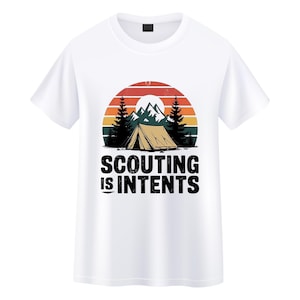 Può includere: T-shirt bianca con grafica a tema campeggio. Il design include una tenda, montagne e alberi sullo sfondo di un tramonto. Il testo "SCOUTING IS INTENTS" è stampato sotto in grassetto, in lettere nere.