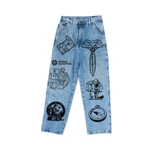 May include: Light blue denim jeans with black graphic illustrations of a map, necktie, backpack, scout, compass, and a person working. The jeans feature the text "WORLD SCOUTING" and are a unique fashion statement.