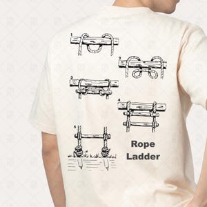 Op de afbeelding: Een crèmekleurig T-shirt met een zwarte afbeelding die laat zien hoe je een touwladder maakt. Het ontwerp bevat genummerde diagrammen en de woorden "Rope Ladder". Het shirt is gemaakt van een zacht, comfortabel materiaal.