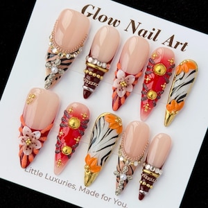 May include: A set of ten press-on nails on a white display card labeled Glow Nail Art and Little Luxuries, Made for You. The nails feature almond and stiletto shapes with designs including zebra stripes, red gradients, floral accents, gold studs, and rhinestones.
