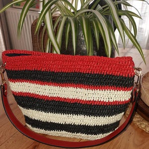 Peut inclure: Sac à main rayé rouge, noir et blanc. Le sac est doté d'une bandoulière rouge et d'une quincaillerie dorée. Le sac est fait d'une matière tissée et l'intérieur est noir.