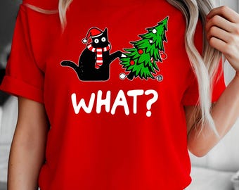May include: Red t-shirt featuring a black cat wearing a Santa hat and scarf, interacting with a Christmas tree. The word "WHAT?" is printed in white below the cat and tree. The shirt is a short-sleeved style.