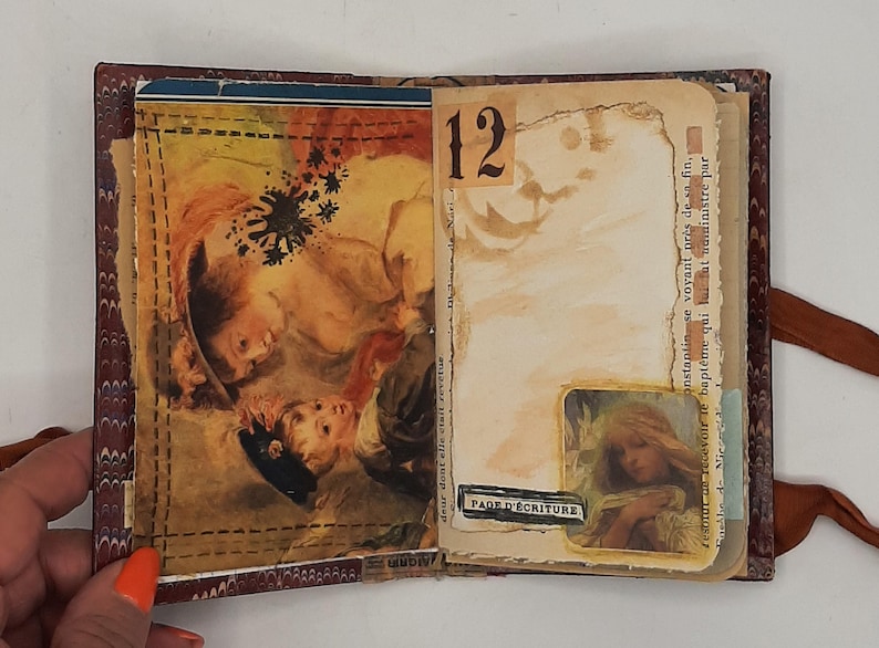 May include: Open journal with vintage-style pages. One page features a detailed illustration of children, while the facing page has the number 12 and a small image. The journal is bound with a brown ribbon.