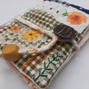 Peut inclure: Un petit journal en tissu fait main avec une couverture en patchwork vert, blanc et orange. Le journal est fermé par un cordon blanc et possède une perle en bois et un bouton en métal.