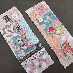 Peut inclure: Deux marque-pages en tissu faits main avec un design patchwork. Les marque-pages présentent une variété de motifs floraux, d'oiseaux et d'autres embellissements. Les marque-pages sont cousus avec un bord festonné et ont un bouton blanc sur chacun.