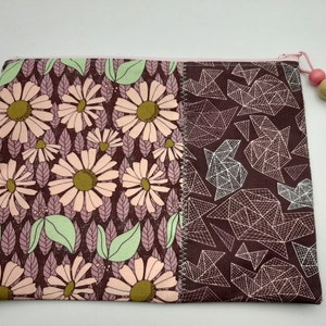 May include: A brown zippered pouch with a floral print on one side and a geometric pattern on the other. The pouch has a pink zipper and a pink and brown tassel.