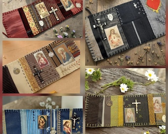 May include: A collection of five fabric prayer books featuring stitched panels, religious imagery, and metal crucifixes. Each book displays varied textile textures, embroidered details, and small metallic charms attached to the fabric pages.