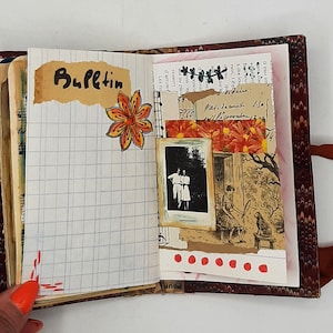 May include: Open journal with a patterned cover, displaying a grid-lined page with the word "Bulletin" and a floral sticker. Other pages feature a black and white photo, floral accents, and handwritten notes. A brown ribbon is attached.