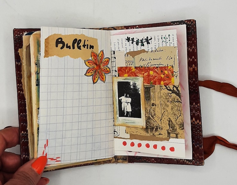 May include: Open journal with a patterned cover, displaying a grid-lined page with the word "Bulletin" and a floral sticker. Other pages feature a black and white photo, floral accents, and handwritten notes. A brown ribbon is attached.