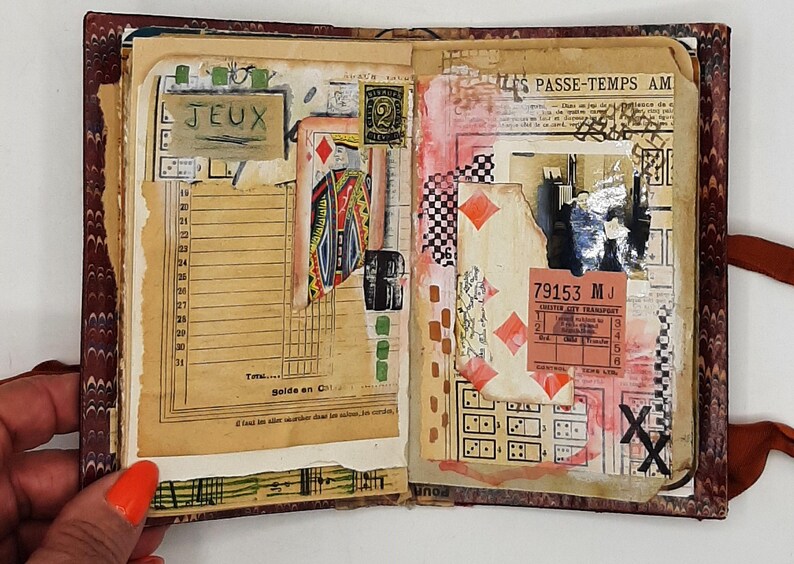 May include: Open journal with collaged pages featuring vintage ephemera. Includes playing card imagery, a postage stamp, and the word "JEUX". The pages are adorned with red, black, and white accents, and a ticket stub.