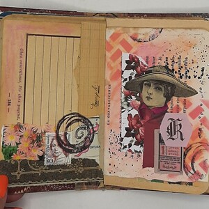 May include: Open vintage journal with aged paper pages. Features a collage of stamps, floral accents, and a portrait of a woman in a hat. Includes handwritten text and decorative elements.