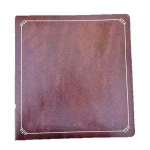May include: A square, burgundy-colored photo album with a textured surface. The album has a gold-colored border with decorative corner accents. The album is closed and appears to be new.