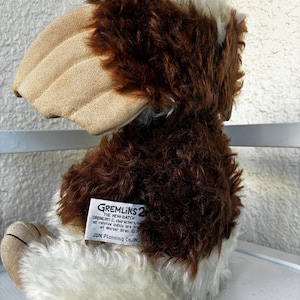 May include: A plush toy character from Gremlins 2 featuring brown and white faux fur, large tan ears, and a white tag on the back that reads GREMLINS 2 THE NEW BATCH, all related indicia are trademarks of Warner Bros. JUN Planning Co., INC.
