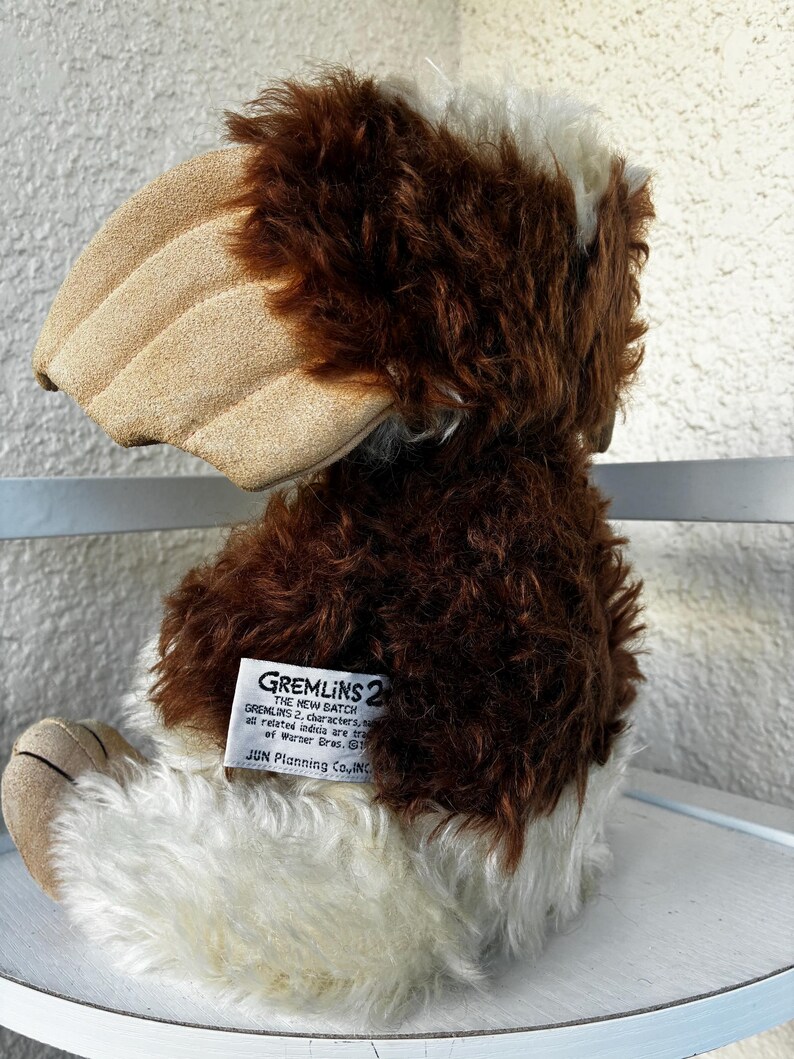 May include: A plush toy character from Gremlins 2 featuring brown and white faux fur, large tan ears, and a white tag on the back that reads GREMLINS 2 THE NEW BATCH, all related indicia are trademarks of Warner Bros. JUN Planning Co., INC.