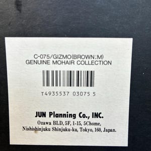 May include: A rectangular white product label on a black background with the text C-075/GIZMO(BROWN;M) GENUINE MOHAIR COLLECTION, a barcode, the number T4935537 03075 5, and the company name JUN Planning Co., INC. with its Tokyo, Japan address.