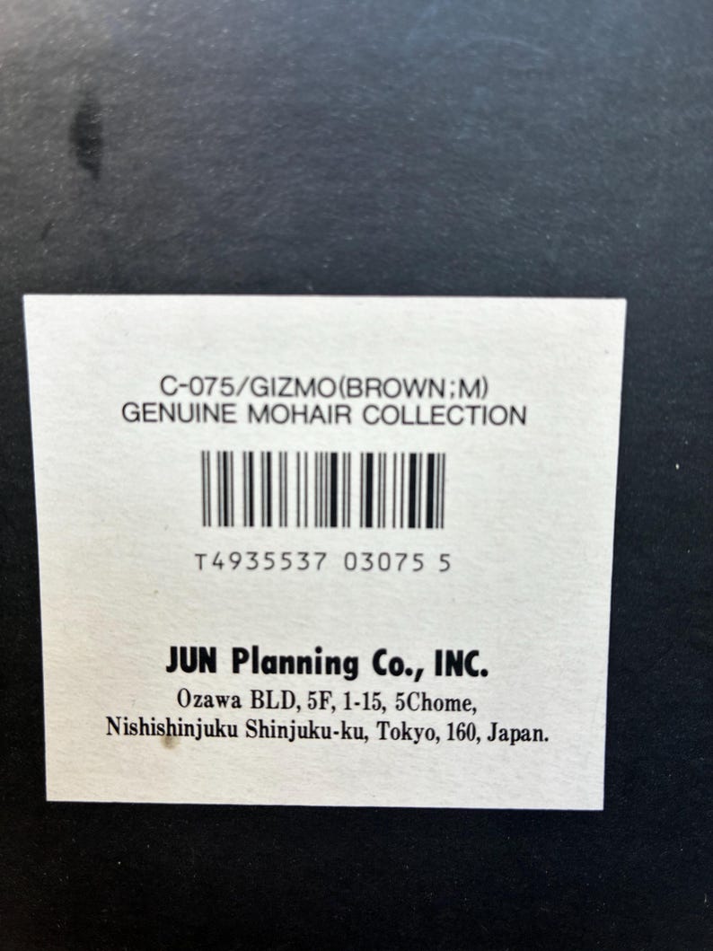 May include: A rectangular white product label on a black background with the text C-075/GIZMO(BROWN;M) GENUINE MOHAIR COLLECTION, a barcode, the number T4935537 03075 5, and the company name JUN Planning Co., INC. with its Tokyo, Japan address.