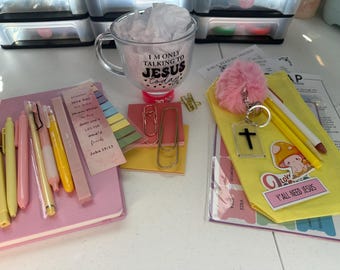 May include: A pink journal with a yellow and pink bookmark, a mug with the text "I'm only talking to Jesus today", a yellow pouch with the text "Y'all need Jesus", and a variety of pens and paper clips.