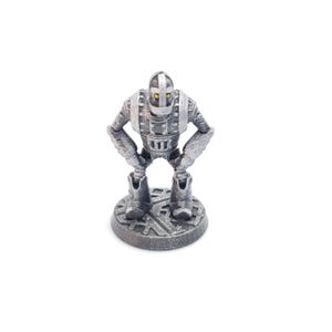May include: A silver-colored robot figurine with a detailed design. The robot has a helmet, a rectangular chest, and is standing on a circular base. The robot's arms are bent at the elbows, and its eyes are yellow.