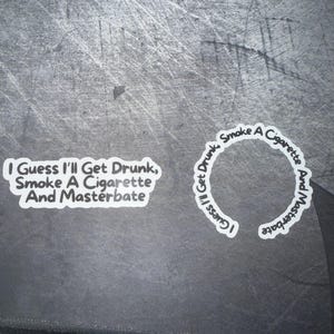 May include: Two white stickers with black text on a gray surface. One sticker reads "I Guess I'll Get Drunk, Smoke A Cigarette And Masterbate." The other sticker is circular and has the same text.